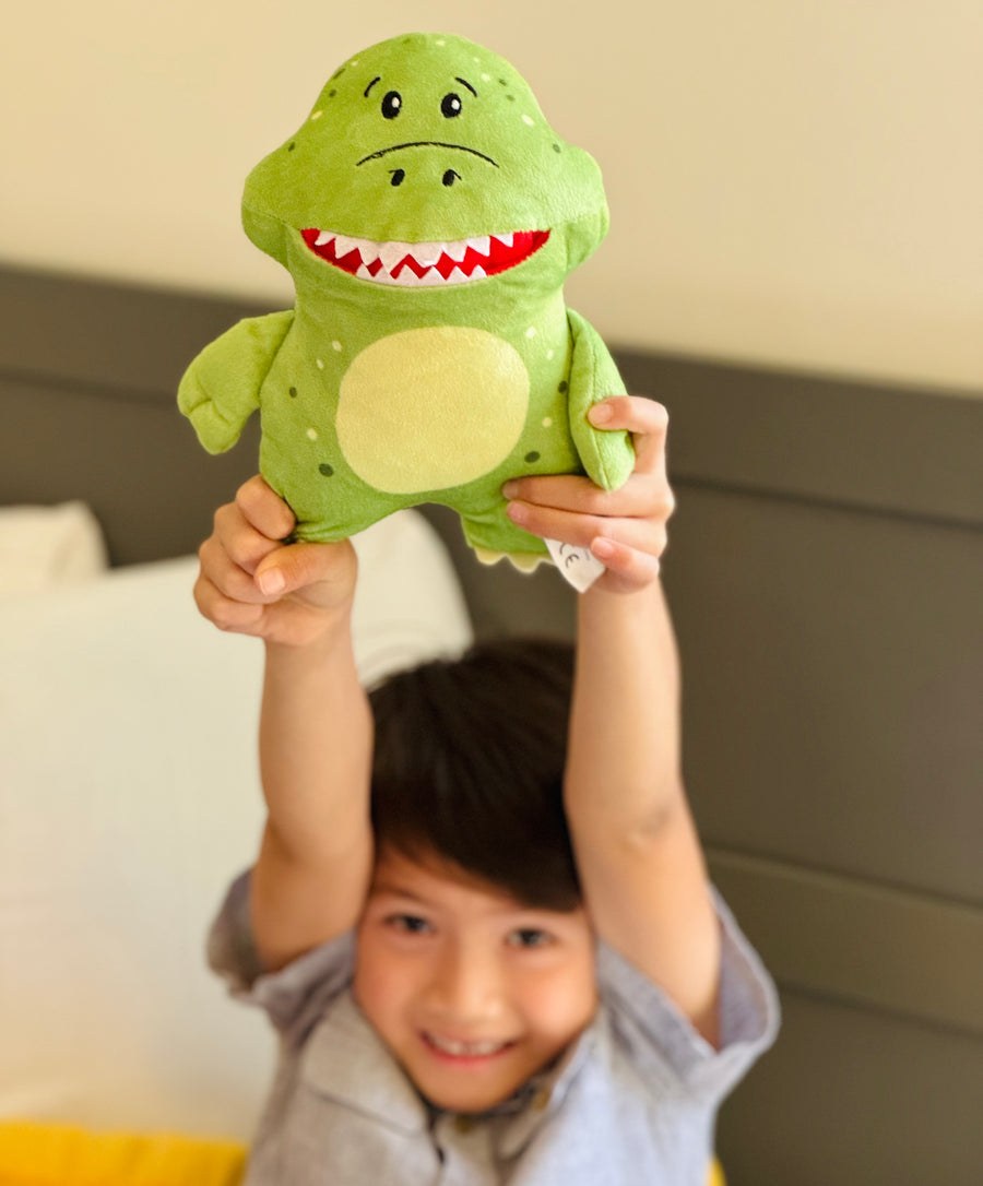 boy hold tooth fairy tooth pillow. the pillow is a t-rex dinosaur